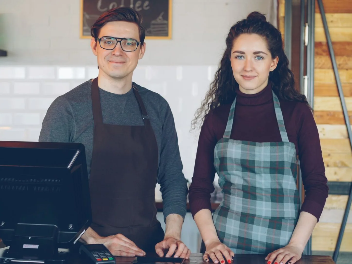 Two smiling cafe staff in aprons standing behind the counter
